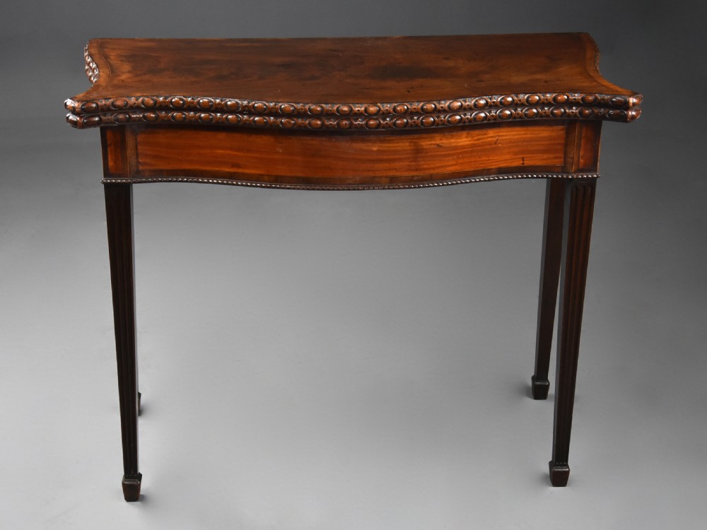 An 18th-century mahogany fold-over card table featuring a serpentine front, carved egg-and-dart rim moulding, and straight fluted legs. View V