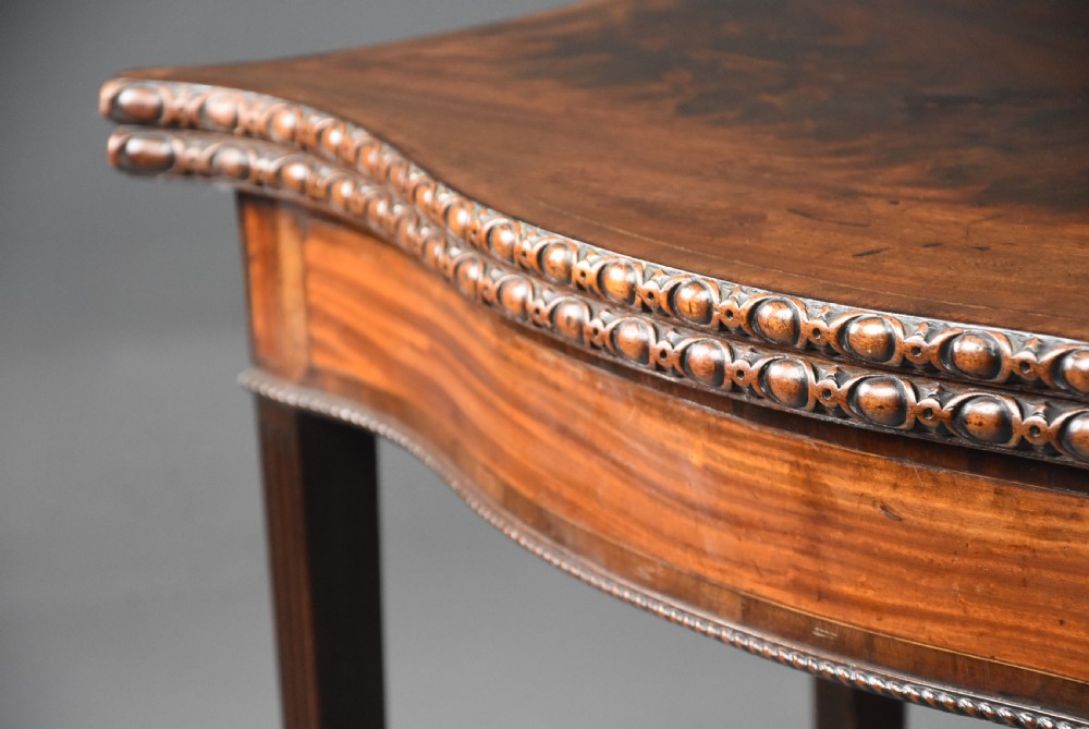 An 18th-century mahogany fold-over card table featuring a serpentine front, carved egg-and-dart rim moulding, and straight fluted legs. View VII