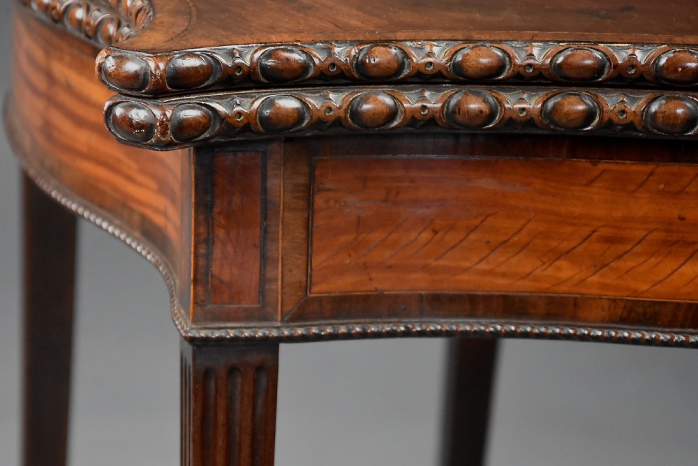 An 18th-century mahogany fold-over card table featuring a serpentine front, carved egg-and-dart rim moulding, and straight fluted legs. View VIII