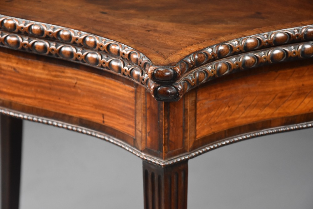An 18th-century mahogany fold-over card table featuring a serpentine front, carved egg-and-dart rim moulding, and straight fluted legs. View IX