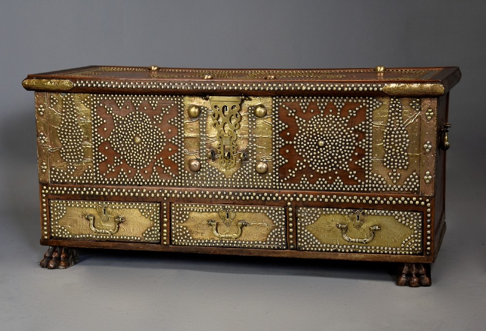 A mid-19th century Zanzibar wooden chest featuring intricate brass studding, pierced brass plates, three lower drawers, and carved feet.