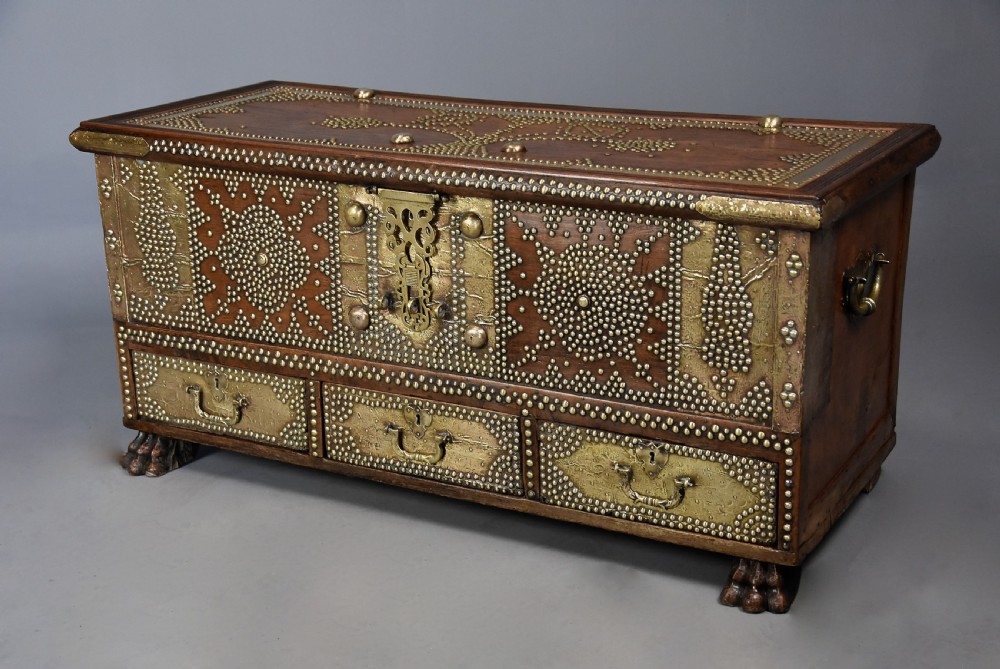 A mid-19th century Zanzibar wooden chest featuring intricate brass studding, pierced brass plates, three lower drawers, and carved feet. View II