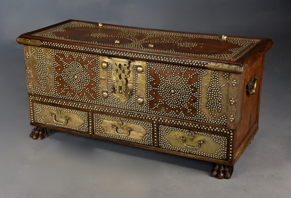 A mid-19th century Zanzibar wooden chest featuring intricate brass studding, pierced brass plates, three lower drawers, and carved feet. View III