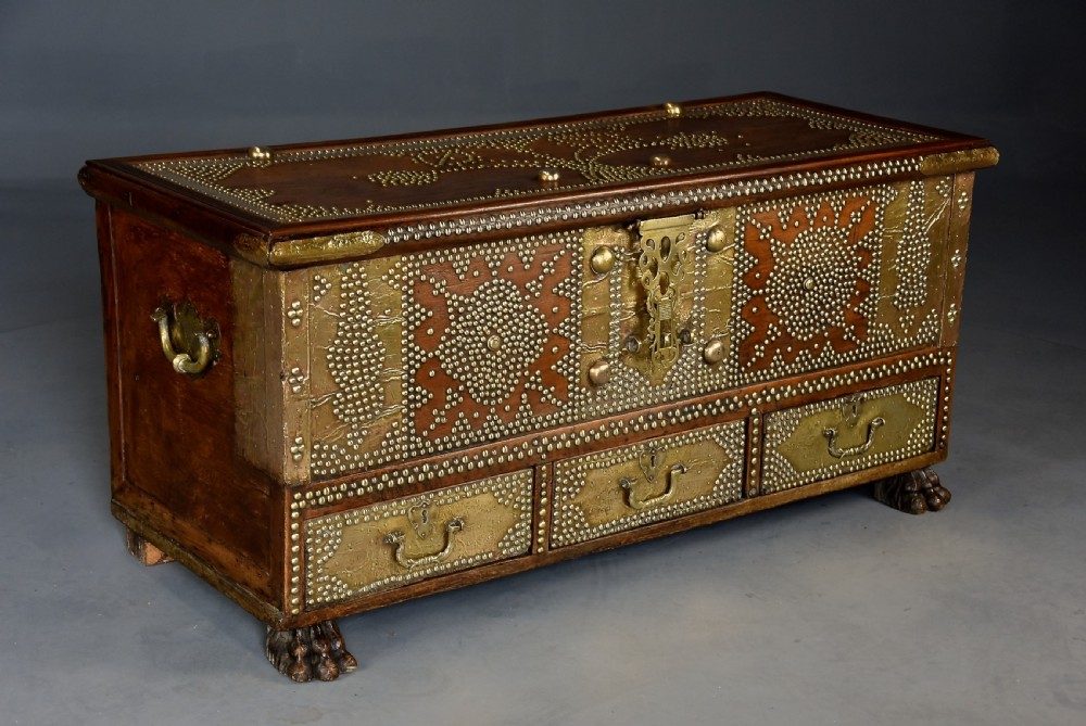 A mid-19th century Zanzibar wooden chest featuring intricate brass studding, pierced brass plates, three lower drawers, and carved feet. View IV