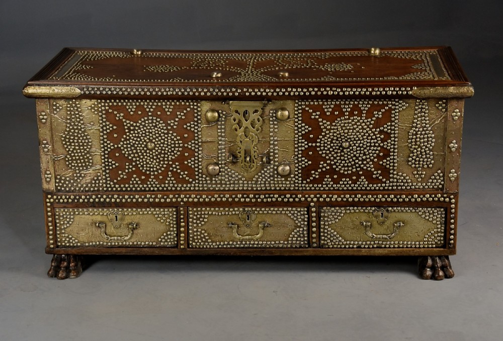 A mid-19th century Zanzibar wooden chest featuring intricate brass studding, pierced brass plates, three lower drawers, and carved feet. View V