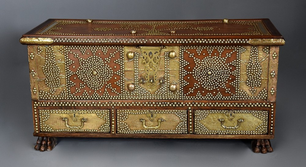 A mid-19th century Zanzibar wooden chest featuring intricate brass studding, pierced brass plates, three lower drawers, and carved feet. View VI