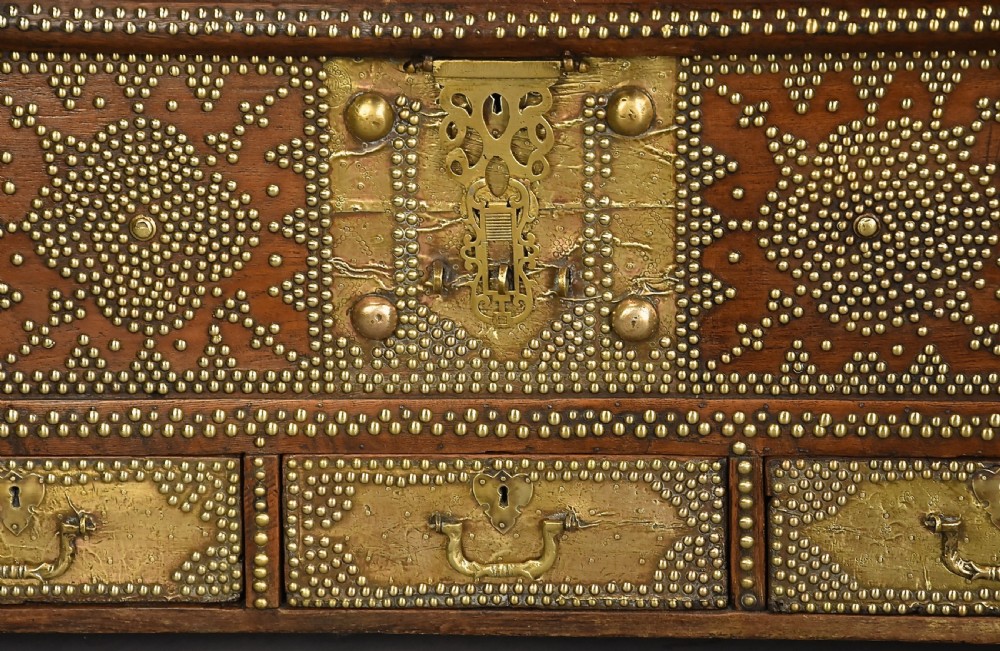 A mid-19th century Zanzibar wooden chest featuring intricate brass studding, pierced brass plates, three lower drawers, and carved feet. View VII
