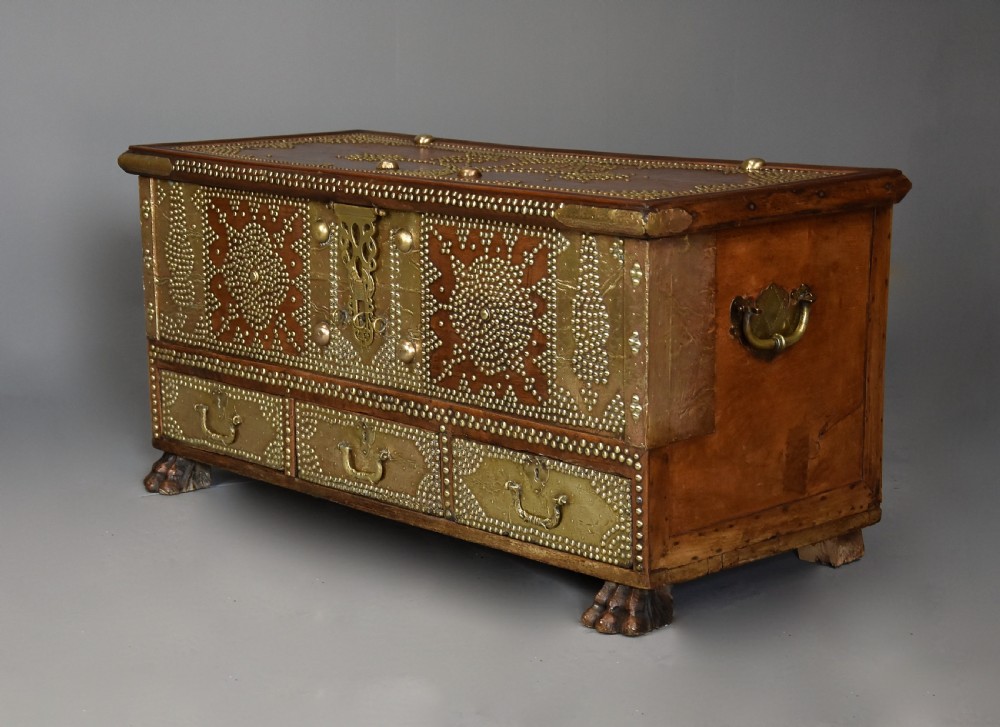 A mid-19th century Zanzibar wooden chest featuring intricate brass studding, pierced brass plates, three lower drawers, and carved feet. View VIII