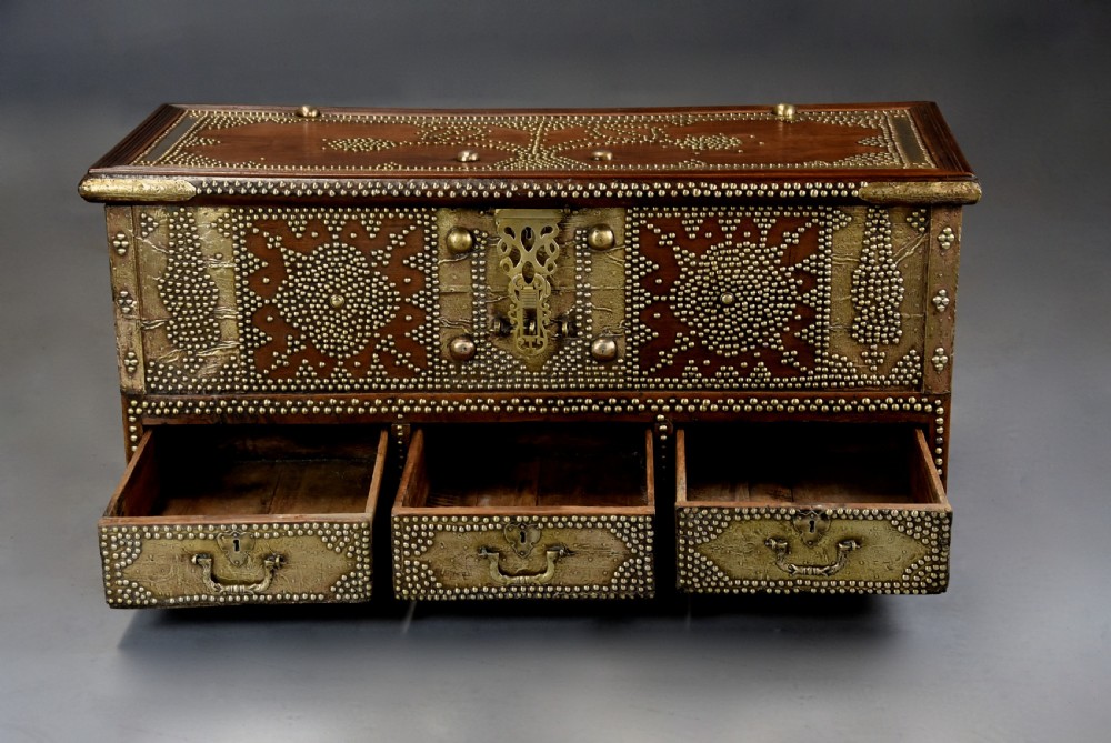 A mid-19th century Zanzibar wooden chest featuring intricate brass studding, pierced brass plates, three lower drawers, and carved feet. View IX