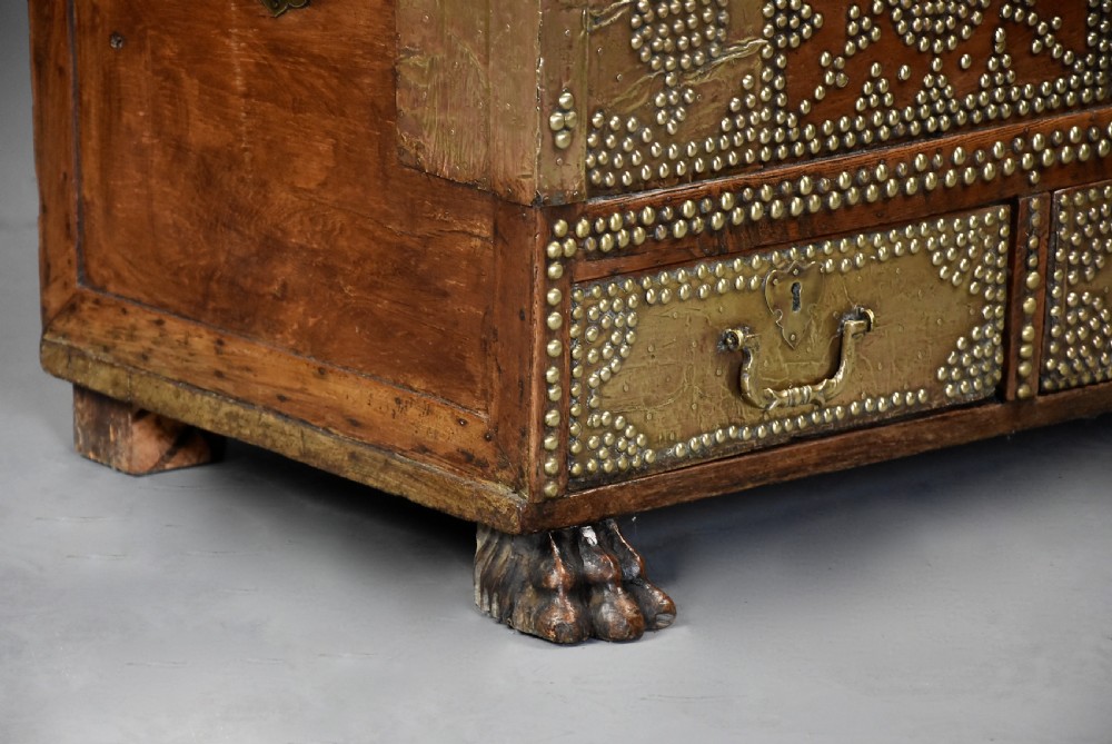 A mid-19th century Zanzibar wooden chest featuring intricate brass studding, pierced brass plates, three lower drawers, and carved feet. View X