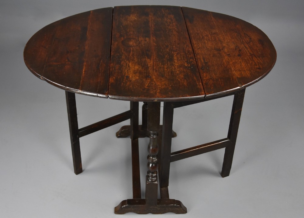 A seventeenth-century dark oak gateleg table shown with both drop-down leaves extended to form an oval tabletop supported on turned legs.