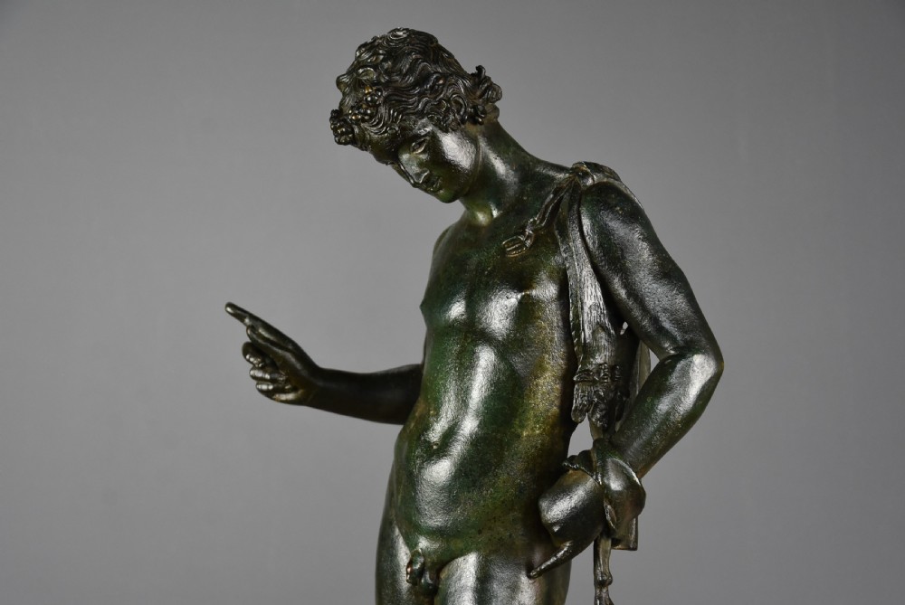 A late 19th-century patinated bronze figure of a standing classical youth with a raised right hand, mounted on a circular moulded base. View XI