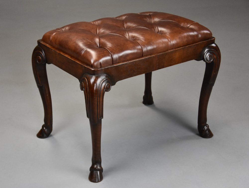 A late 19th-century Queen Anne style walnut stool featuring a deep-buttoned brown leather seat and carved cabriole legs with hoof feet. View V
