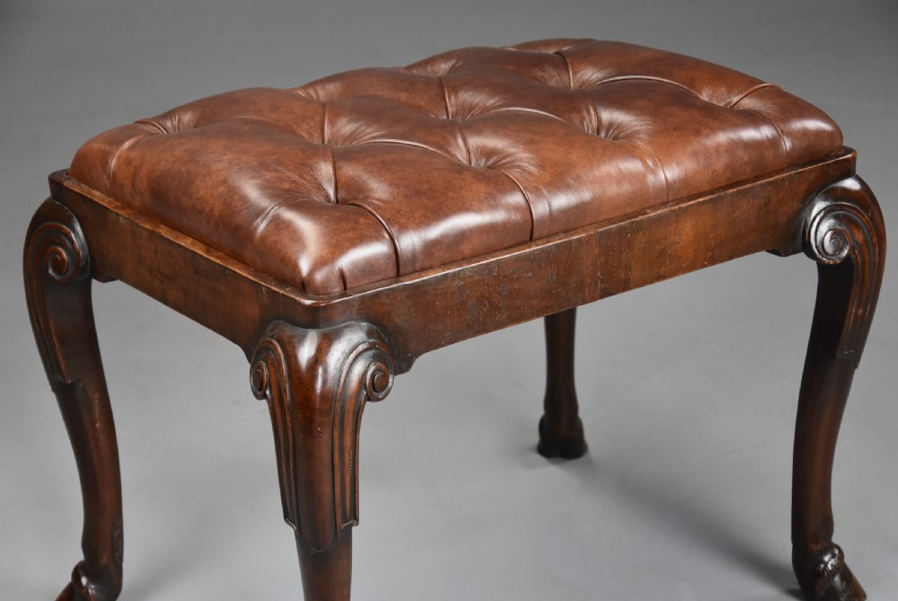 A late 19th-century Queen Anne style walnut stool featuring a deep-buttoned brown leather seat and carved cabriole legs with hoof feet. View VI