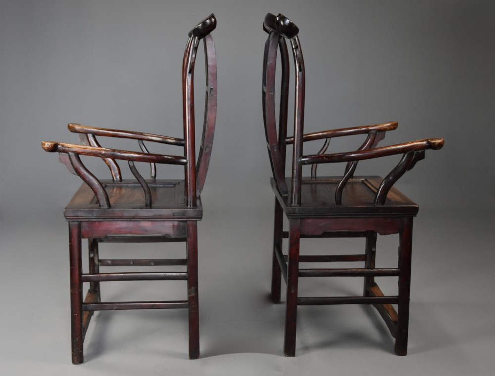 A pair of late 19th-century Chinese armchairs crafted from dark red lacquered elm with shaped yokeback top rails and hand-carved central splats. View X