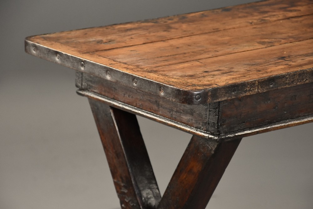 An early 19th-century sycamore tavern table featuring an X-frame trestle base, plank top, and metal stretcher rod. View IX
