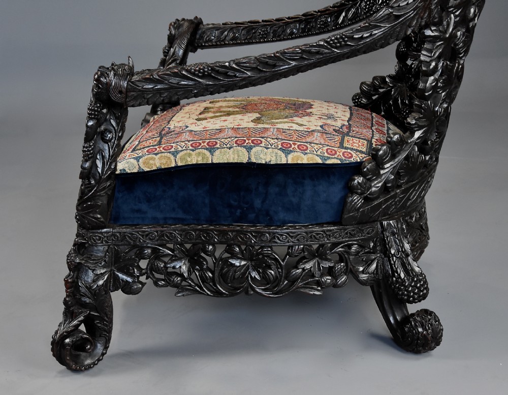 A 19th-century Anglo-Indian carved blackwood armchair featuring an intricately pierced foliate backrest and an embroidered fabric seat cushion. View X