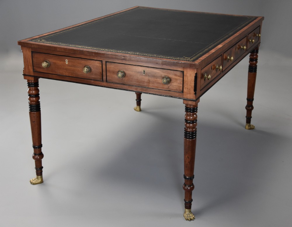 A Regency mahogany writing table featuring a dark leather insert, six drawers with brass knobs, and reeded turned legs with brass paw feet. View IV