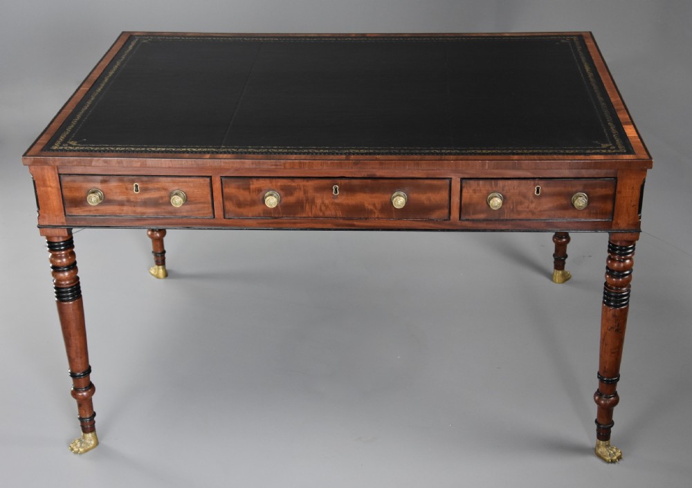 A Regency mahogany writing table featuring a dark leather insert, six drawers with brass knobs, and reeded turned legs with brass paw feet. View V