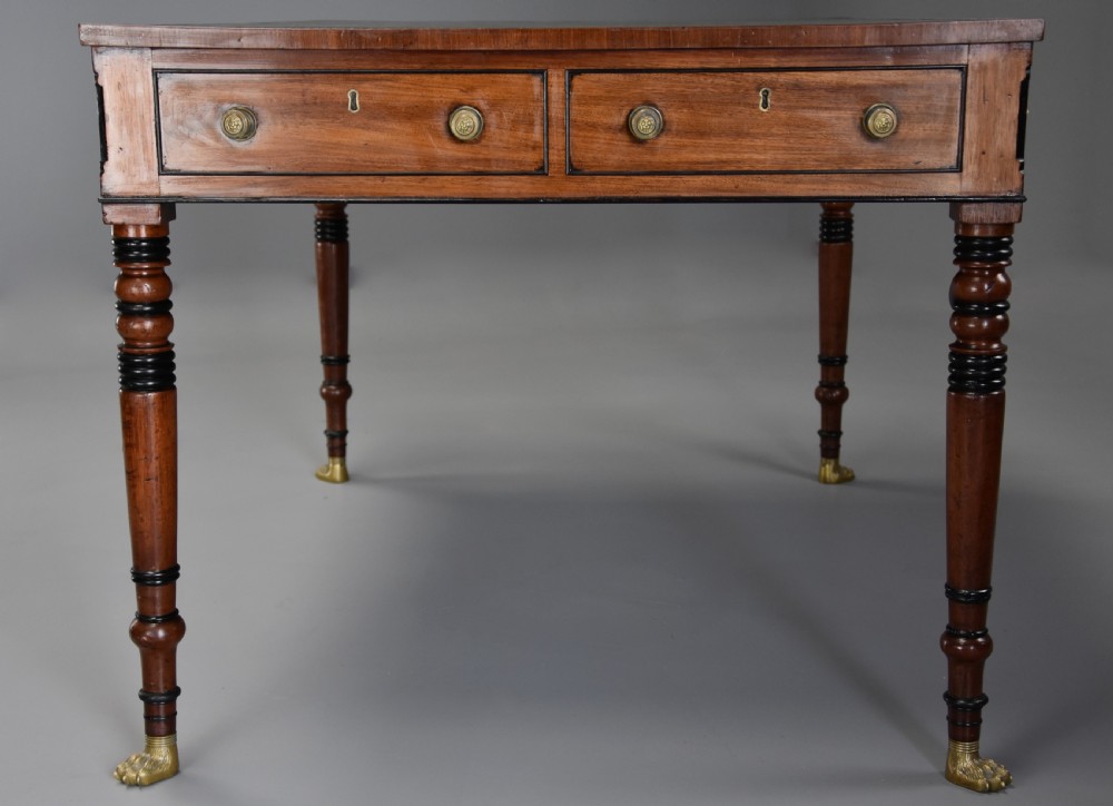 A Regency mahogany writing table featuring a dark leather insert, six drawers with brass knobs, and reeded turned legs with brass paw feet. View VI