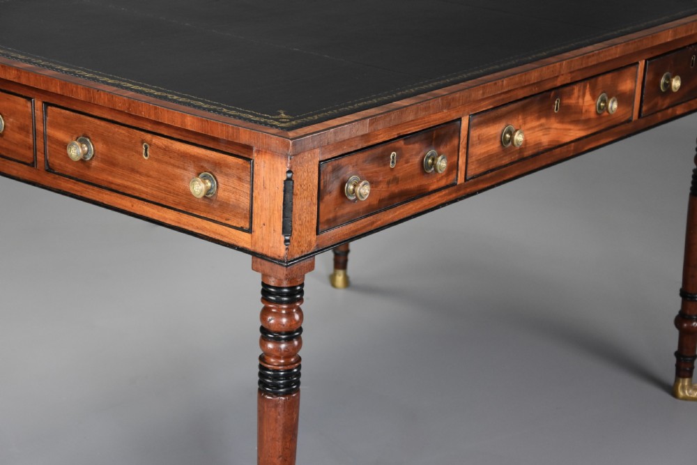 A Regency mahogany writing table featuring a dark leather insert, six drawers with brass knobs, and reeded turned legs with brass paw feet. View VII