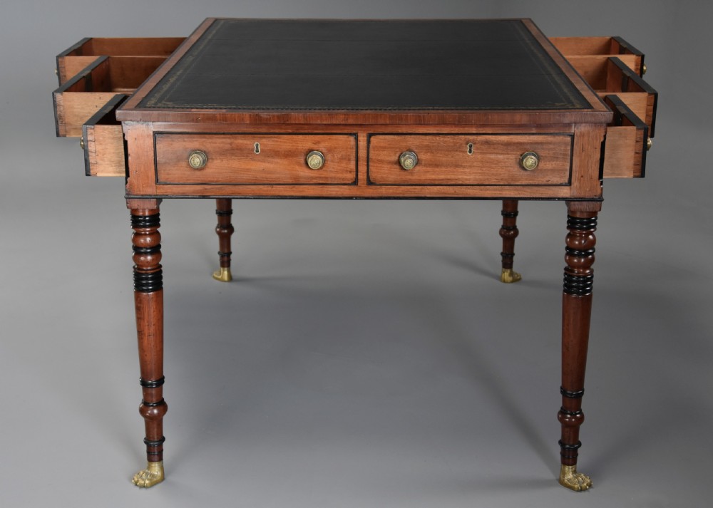 A Regency mahogany writing table featuring a dark leather insert, six drawers with brass knobs, and reeded turned legs with brass paw feet. View IX