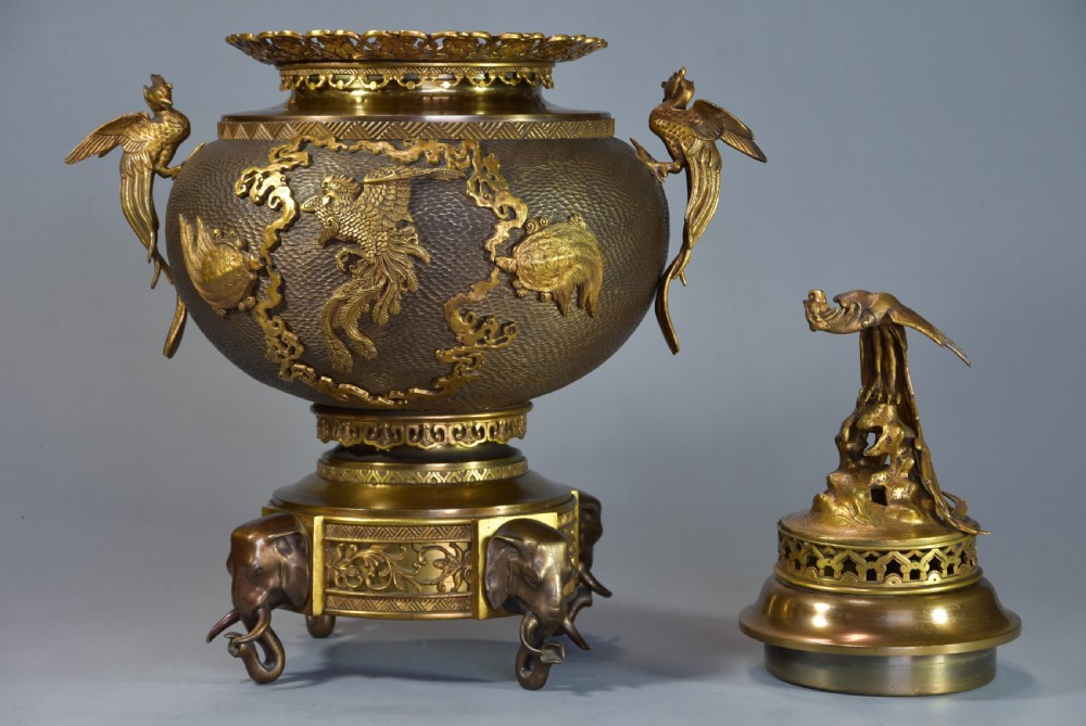 A late nineteenth-century three-piece French Japonisme bronze garniture set featuring a central incense burner flanked by two tall urns, decorated with gilt dragon reliefs and supported on elephant head feet. View V