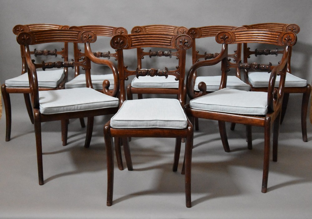 A set of eight antique Regency mahogany dining chairs featuring reeded top rails, carved mid-rails, scrolled armrests, and pale blue upholstered seats.
