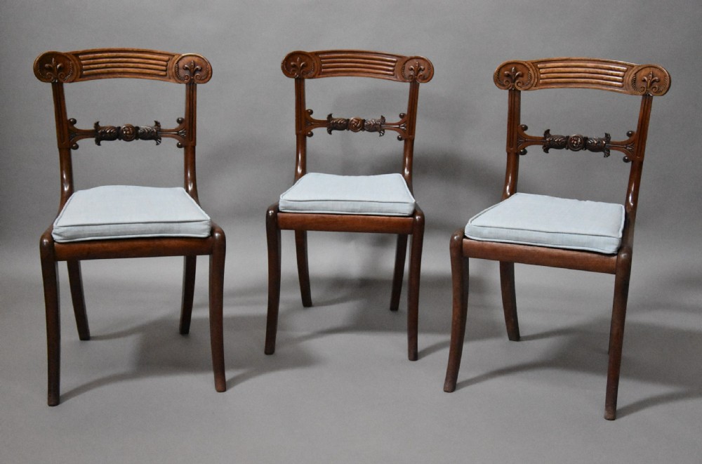 A set of eight antique Regency mahogany dining chairs featuring reeded top rails, carved mid-rails, scrolled armrests, and pale blue upholstered seats. View V