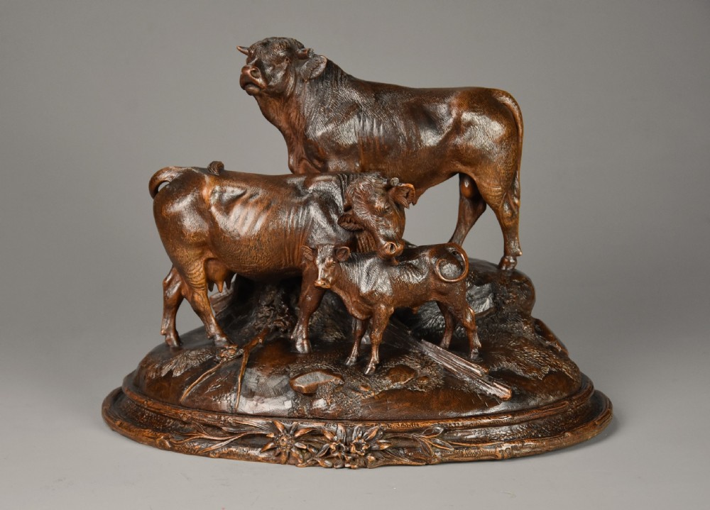A late nineteenth-century dark linden wood sculpture depicting a bull, cow, and calf standing on a naturalistic base with carved edelweiss motifs.