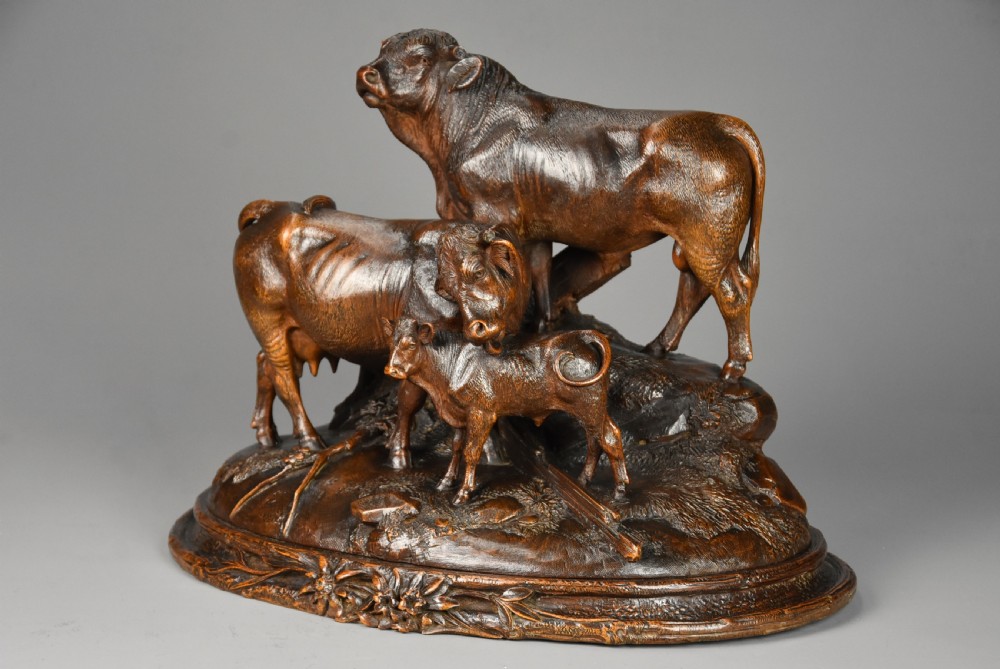 A late nineteenth-century dark linden wood sculpture depicting a bull, cow, and calf standing on a naturalistic base with carved edelweiss motifs. View V