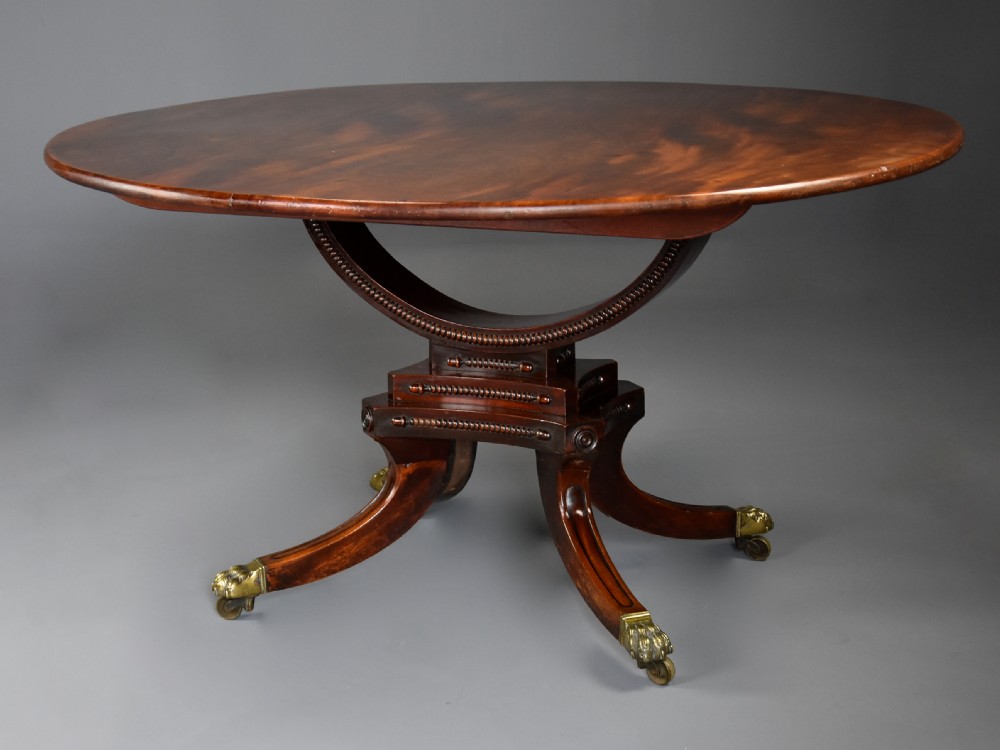 An early nineteenth-century circular mahogany centre table shown tilted upright on a central pedestal with four splayed legs terminating in brass paw castors. View II