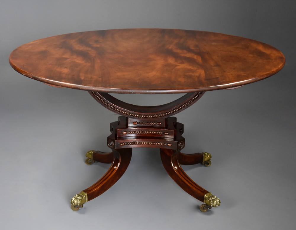 An early nineteenth-century circular mahogany centre table shown tilted upright on a central pedestal with four splayed legs terminating in brass paw castors. View III