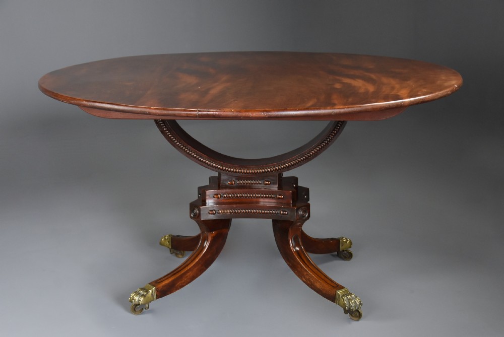 An early nineteenth-century circular mahogany centre table shown tilted upright on a central pedestal with four splayed legs terminating in brass paw castors. View IV