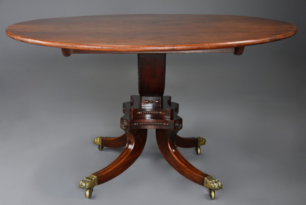 An early nineteenth-century circular mahogany centre table shown tilted upright on a central pedestal with four splayed legs terminating in brass paw castors. View V