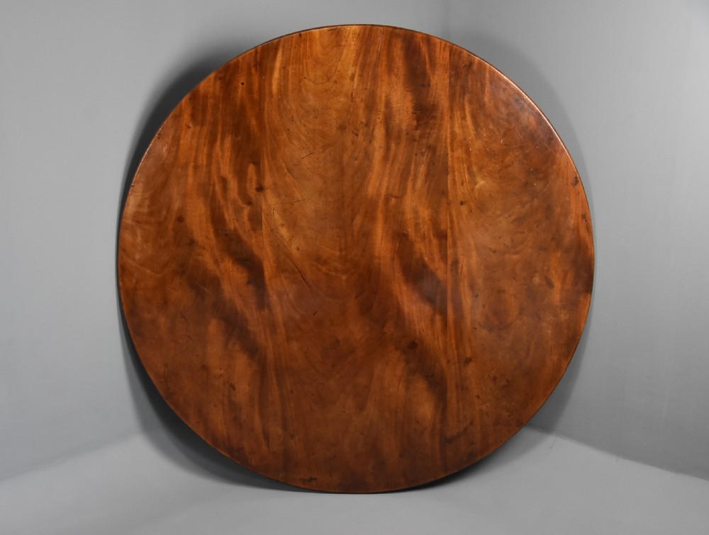 An early nineteenth-century circular mahogany centre table shown tilted upright on a central pedestal with four splayed legs terminating in brass paw castors. View X