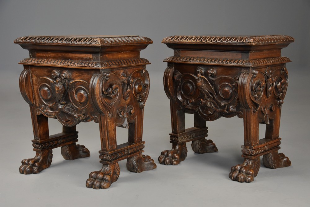 A pair of carved warm brown walnut stools with gadrooned tops, central bird reliefs, scrollwork aprons, and paw feet.