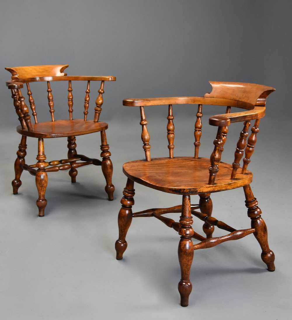 A pair of 19th-century birch smokers bow Windsor armchairs featuring steam-bent armrails, turned spindles, saddle seats, and turned legs with stretchers.