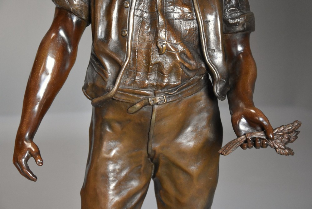 A late 19th-century French bronzed spelter figure depicting a barefoot male farm labourer holding a small bundle of wheat on a moulded base. View VI