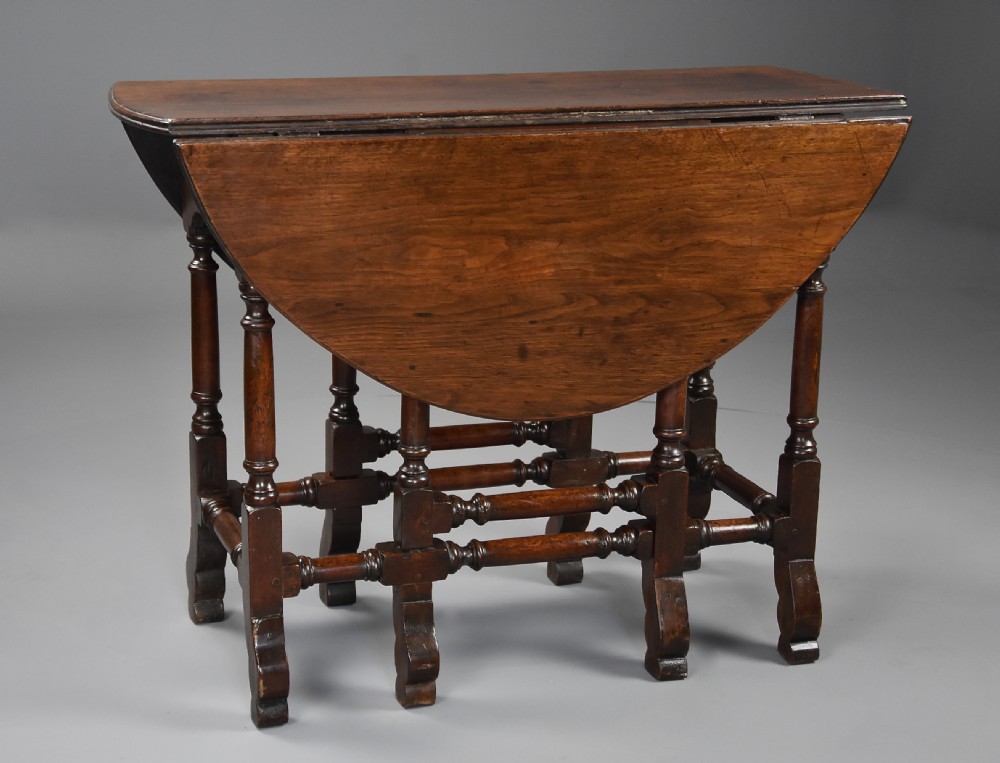 An 18th-century red walnut gateleg table featuring an oval top with two drop leaves, turned legs, box stretchers, and a small drawer with a brass knob. View V