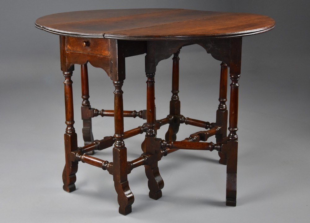 An 18th-century red walnut gateleg table featuring an oval top with two drop leaves, turned legs, box stretchers, and a small drawer with a brass knob. View VII