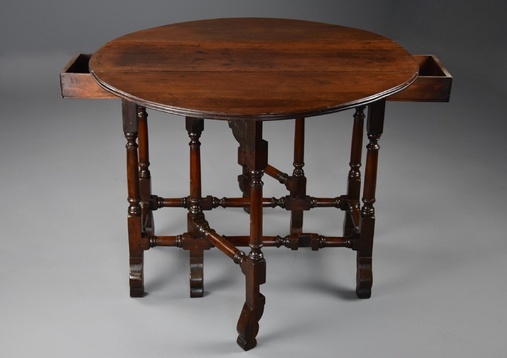 An 18th-century red walnut gateleg table featuring an oval top with two drop leaves, turned legs, box stretchers, and a small drawer with a brass knob. View VIII