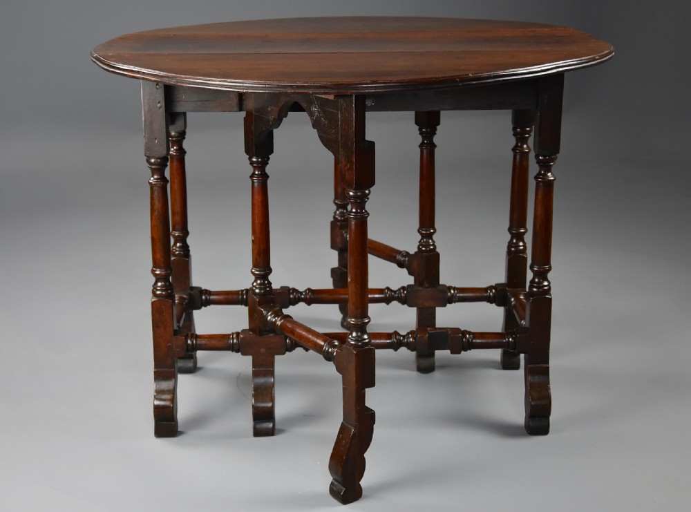 An 18th-century red walnut gateleg table featuring an oval top with two drop leaves, turned legs, box stretchers, and a small drawer with a brass knob. View X