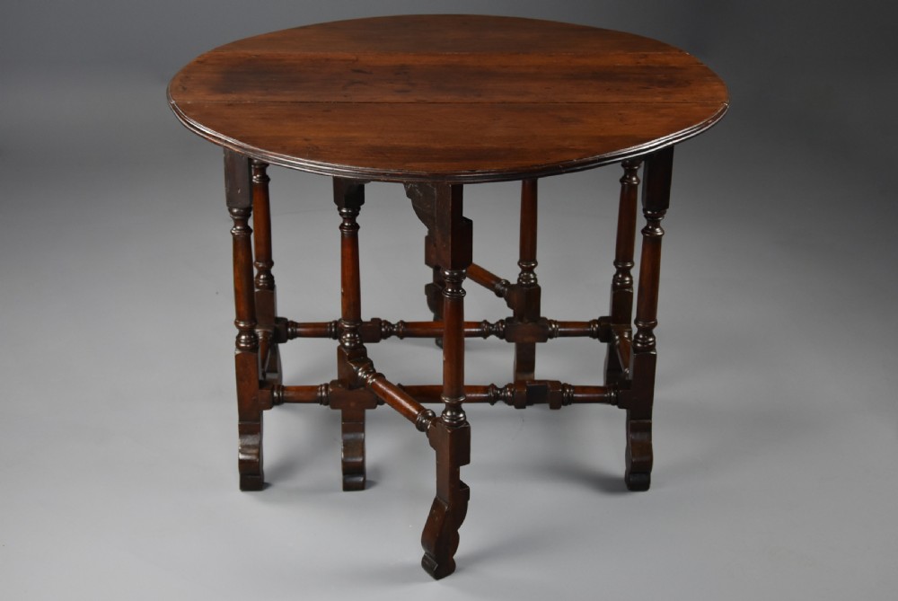 An 18th-century red walnut gateleg table featuring an oval top with two drop leaves, turned legs, box stretchers, and a small drawer with a brass knob. View XI