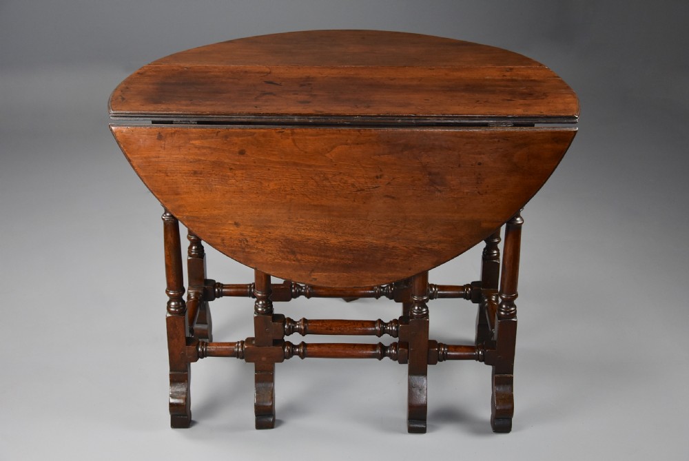 An 18th-century red walnut gateleg table featuring an oval top with two drop leaves, turned legs, box stretchers, and a small drawer with a brass knob. View XII