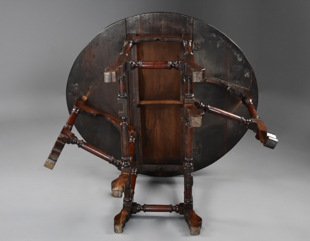 An 18th-century red walnut gateleg table featuring an oval top with two drop leaves, turned legs, box stretchers, and a small drawer with a brass knob. View XIV