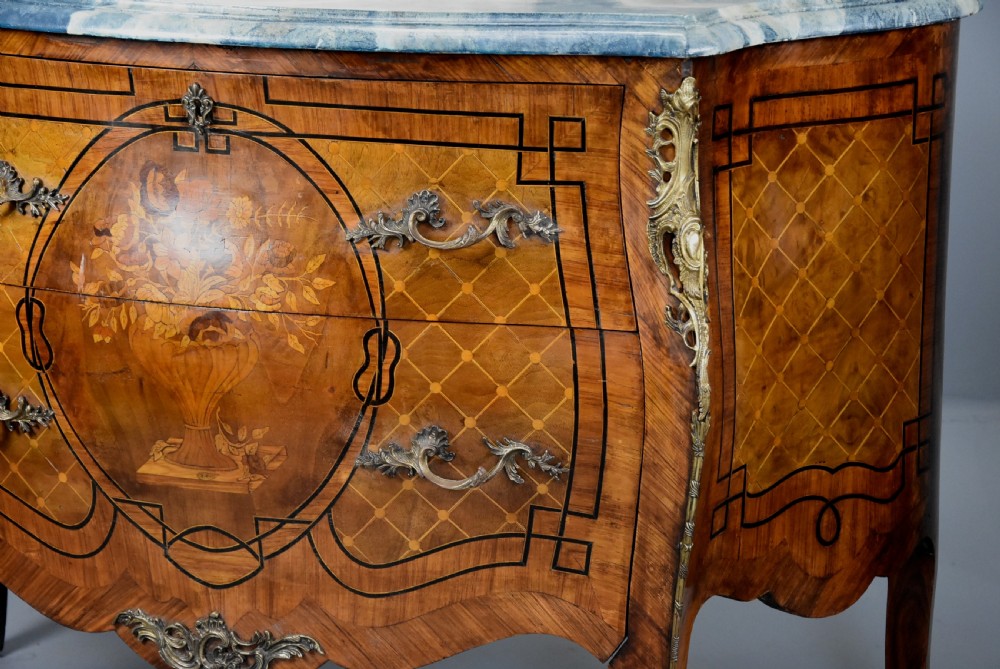 A pair of early twentieth-century French Kingwood bombe commodes featuring floral marquetry panels, serpentine blue marble tops, and detailed gilt-bronze mounts. View VII
