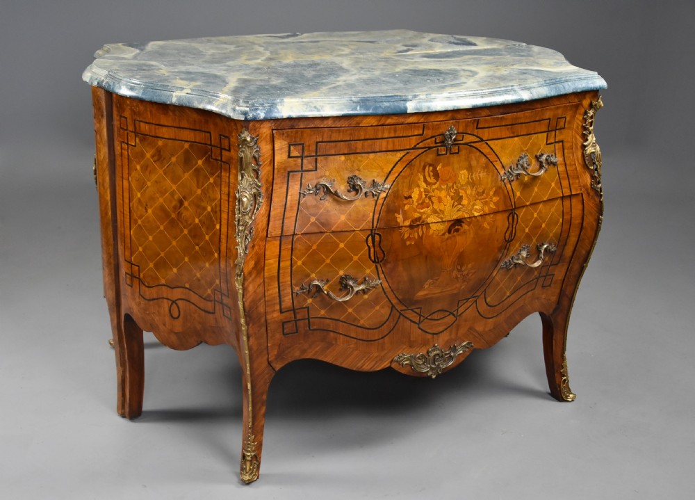 A pair of early twentieth-century French Kingwood bombe commodes featuring floral marquetry panels, serpentine blue marble tops, and detailed gilt-bronze mounts. View X