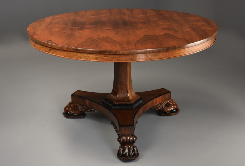 A 19th-century William IV circular rosewood breakfast table featuring a figured veneer top on a faceted pedestal column and a triform plinth base with carved feet. View II