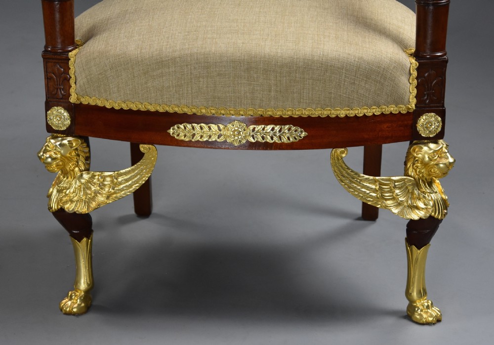 A pair of late nineteenth-century French mahogany open armchairs featuring gilded winged lion front legs and neutral fabric upholstery. View X